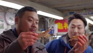 Two Asian men enjoying seafood in a vibrant market.