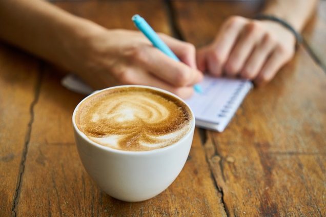 A person writing on a notebook next to a cup of coffee in Apartments in Westpark.